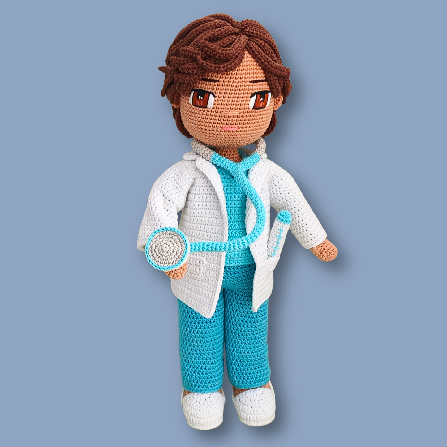 Dr. Thomas amigurumi doll holding the stethoscope chest piece, wearing white doctor coat and turquoise scrubs