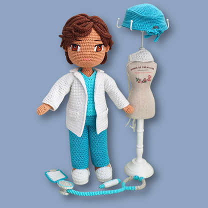 Dr. Thomas crochet doll beside a mini mannequin holding the scrub cap, medical accessories laid out in front