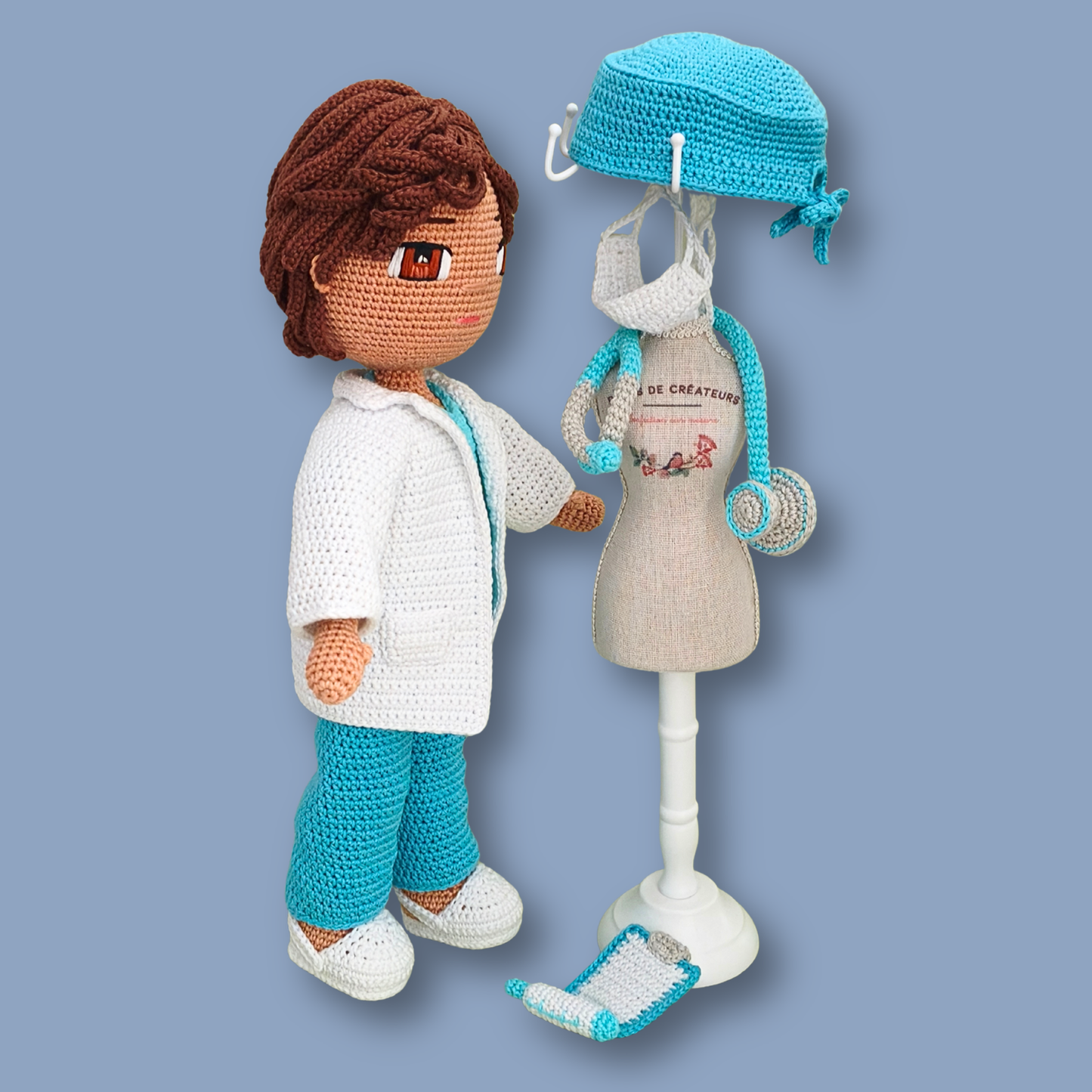 Side view of Dr. Thomas amigurumi doll facing a mini mannequin with scrub cap, face mask, and clipboard